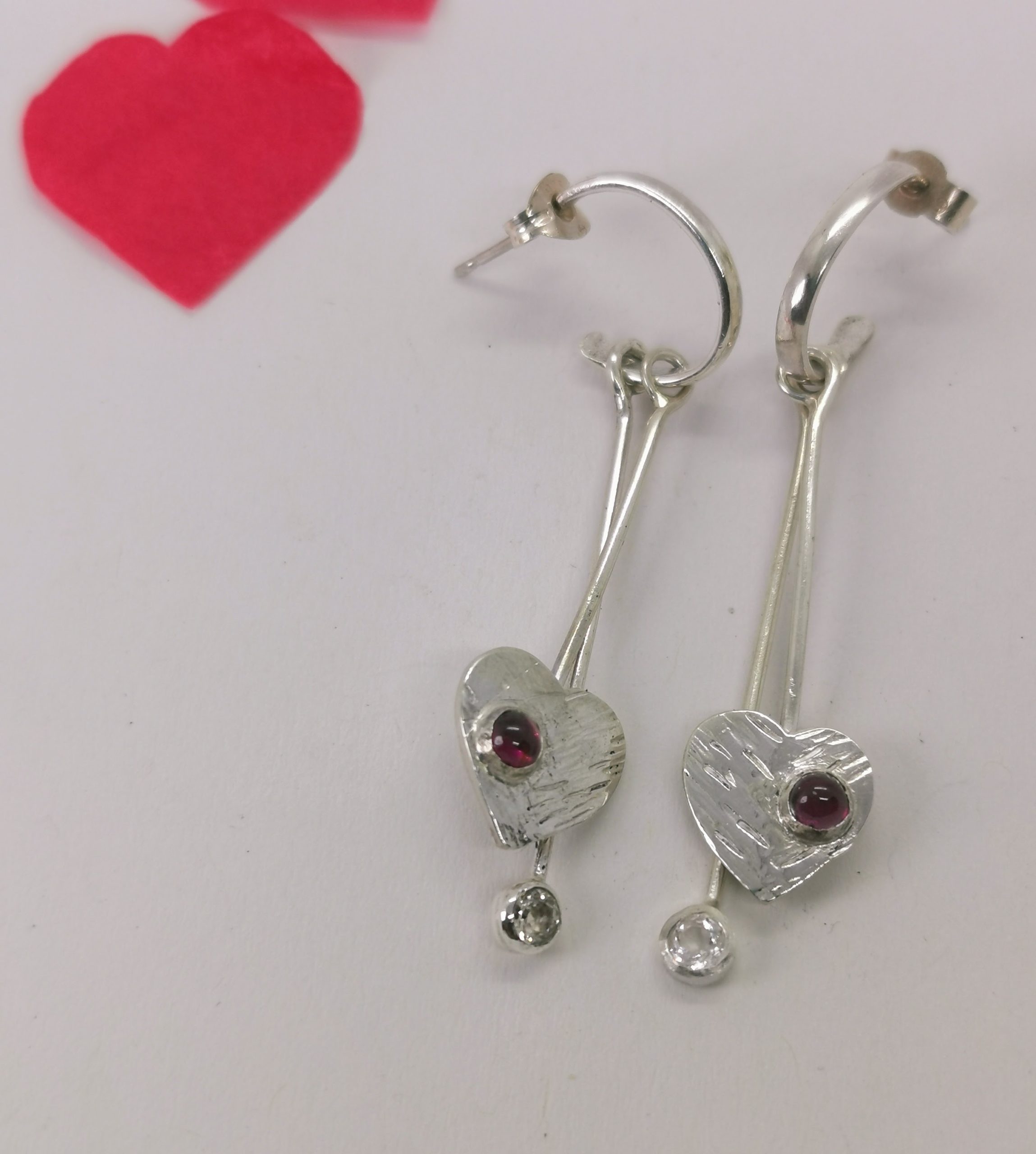 Boucles d'oreilles longue avec un coeur en argent sur lequel il y a un grenat cabochon serti et une tige argent avec une morganite sertie